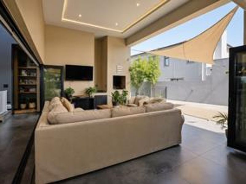 A modern covered patio featuring tiled flooring, a built-in fireplace, recessed ceiling lighting, and seamless access to the garden through large stacking doors.