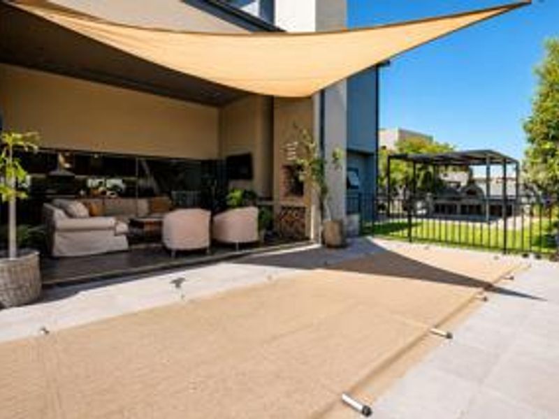 Spacious covered patio featuring a built-in fireplace, shade sail, and seamless transition to the outdoor pool area and garden.