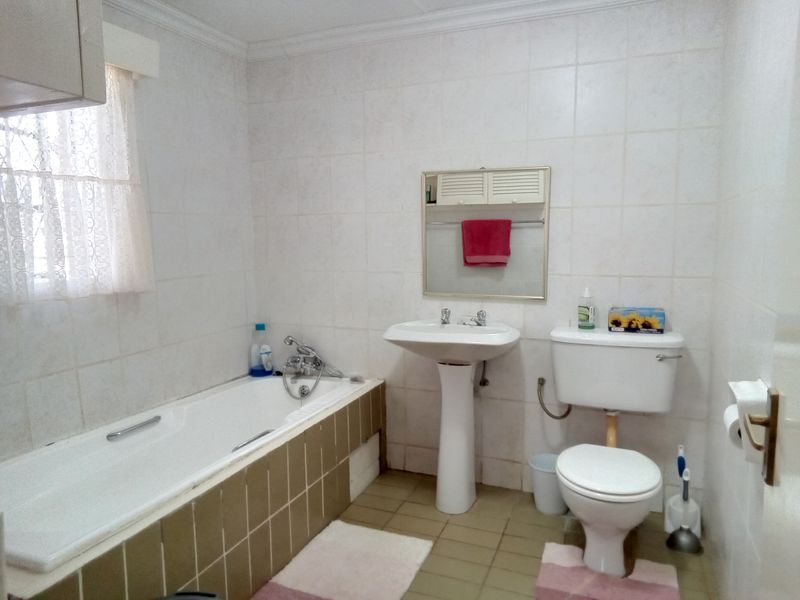 A dated bathroom featuring a standard bathtub, pedestal sink, and toilet with original wall and floor tiling.