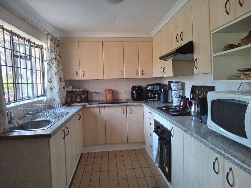 A functional kitchen featuring light wood-finish cabinetry, laminate countertops, built-in oven and hob, and tiled flooring with a window overlooking the exterior.