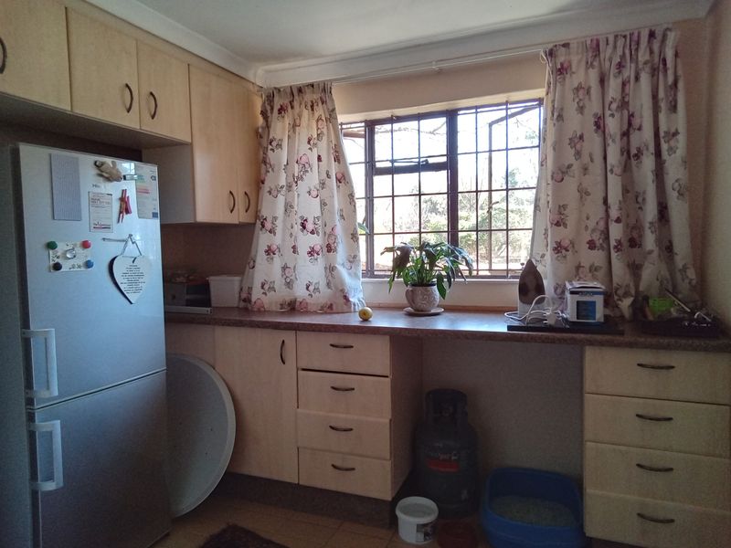 A functional kitchen area featuring light-toned laminate cabinetry, ample counter space, and a window fitted with security bars.