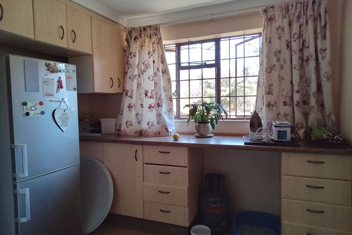 A functional kitchen area featuring light-toned laminate cabinetry, ample counter space, and a window fitted with security bars.