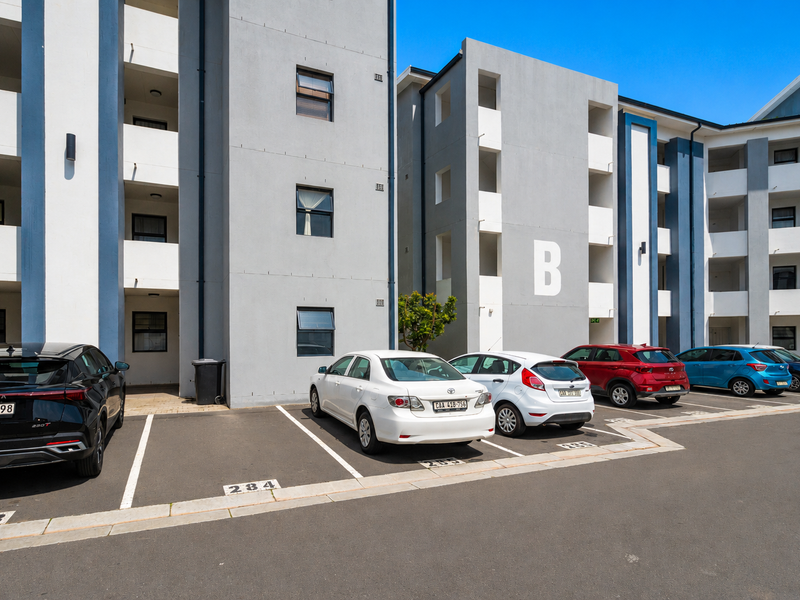 Exterior view of a modern apartment complex featuring a paved parking area and multi-story residential building facade with designated block signage.