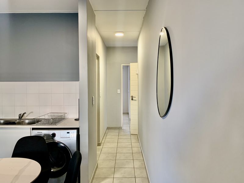 A clean hallway leading to interior rooms, featuring tiled flooring and a partial view of a functional kitchen area with a sink and backsplash.