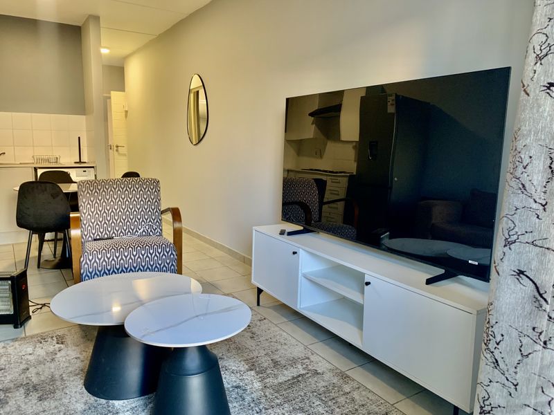 Open-plan living area featuring tiled flooring and a compact kitchen with built-in cabinetry and appliances.