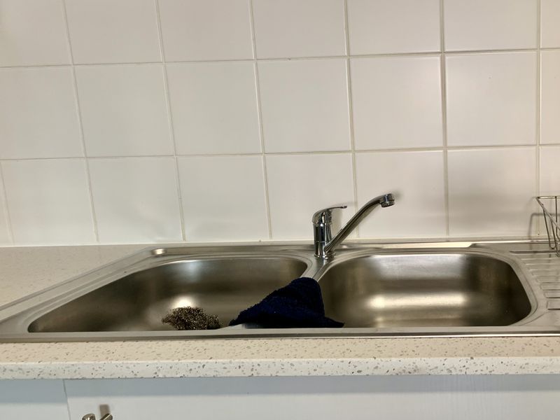 A functional kitchen area featuring a double bowl stainless steel sink with a chrome mixer tap and a clean tiled splashback.