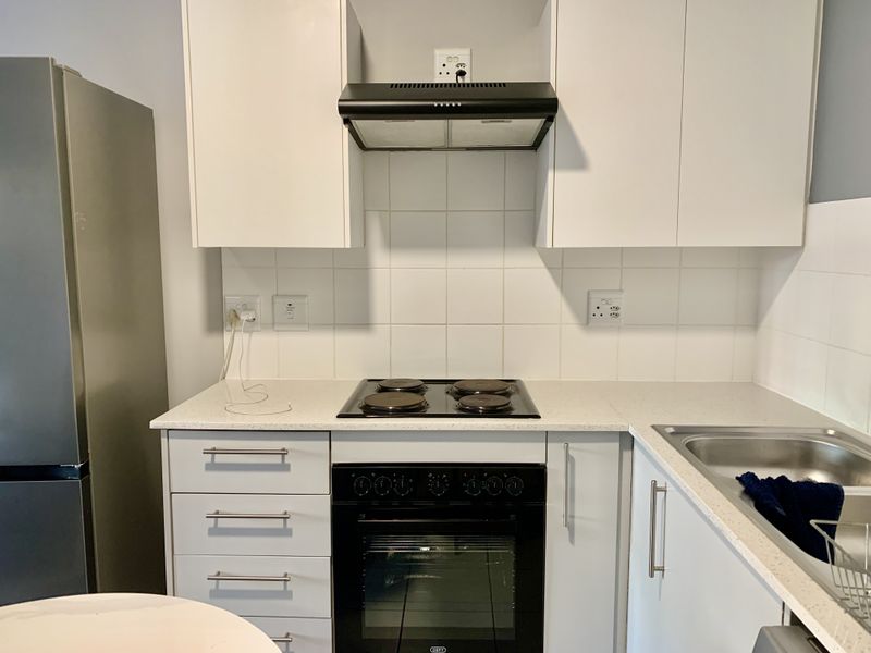 A functional kitchen featuring white cabinetry, stone countertops, a built-in oven with electric hob, and a tiled backsplash.