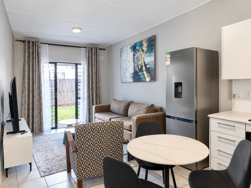 A bright open-plan living and kitchen area featuring tiled floors, modern cabinetry, and a sliding glass door providing direct access to the outdoor space.
