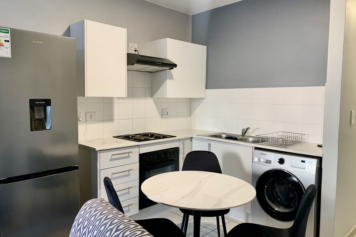A functional kitchen featuring white cabinetry, tiled backsplash, integrated oven and hob, and a stainless steel sink with ample counter space.