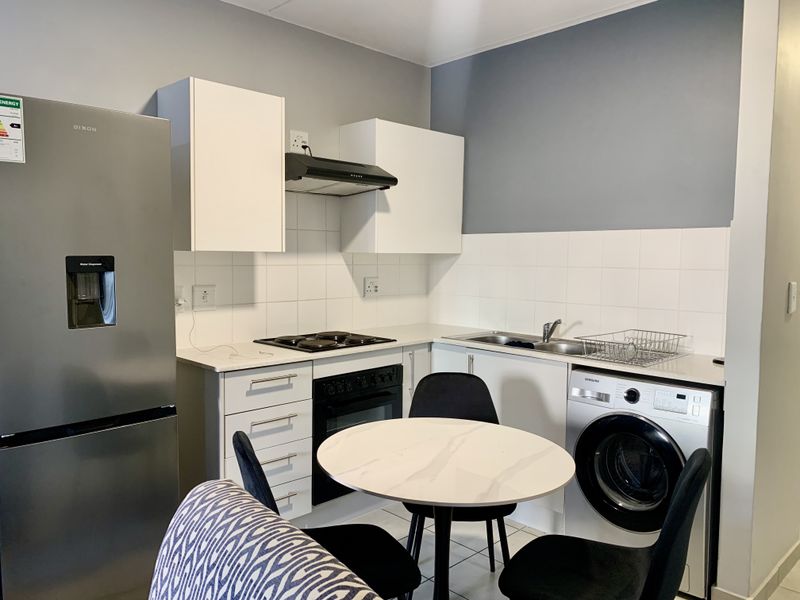 A functional kitchen featuring white cabinetry, tiled backsplash, integrated oven and hob, and a stainless steel sink with ample counter space.