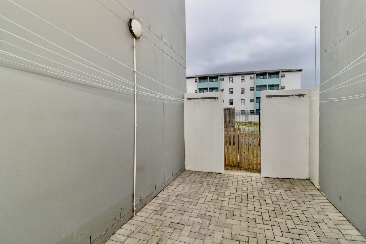 A private paved rear courtyard area featuring boundary walls, a fitted washing line, and a wooden gate providing access.