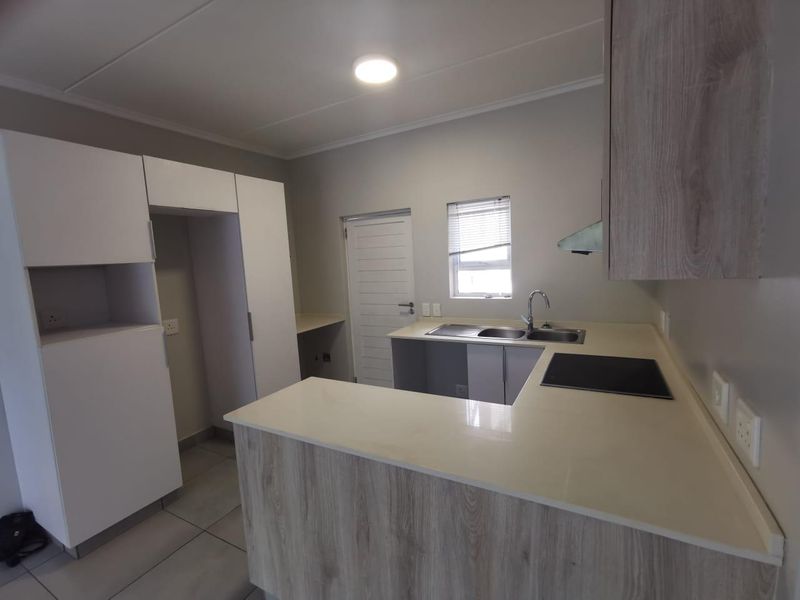 Modern kitchen featuring light wood-grain cabinetry, stone countertops, integrated electric hob, extractor fan, and tiled flooring in a clean, open-plan layout.