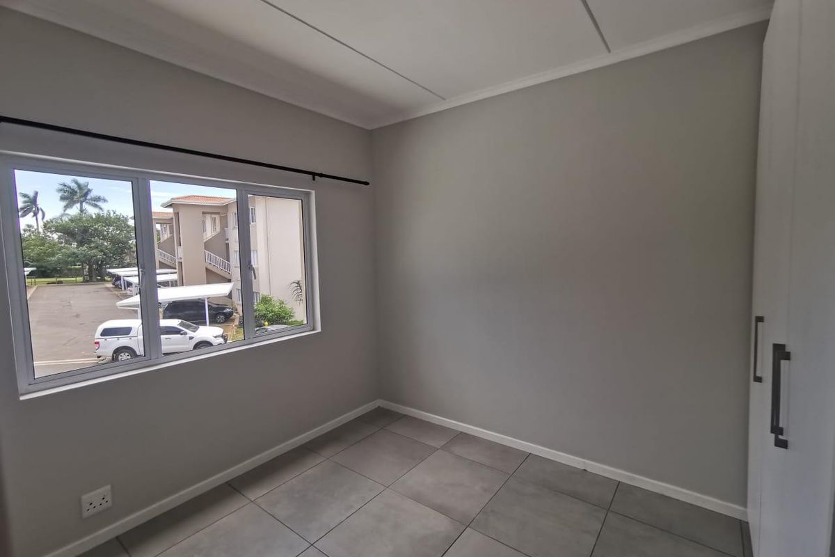 A clean, empty bedroom featuring neutral grey walls, large format floor tiles, and built-in storage cupboards with modern hardware.