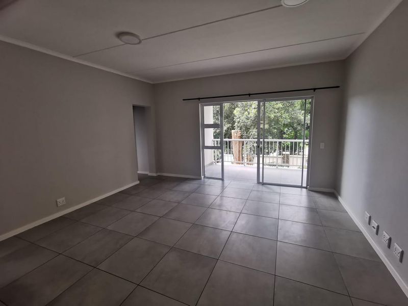 Spacious, empty living area featuring neutral grey floor tiles, recessed lighting, and large sliding glass doors providing direct access to a private balcony.