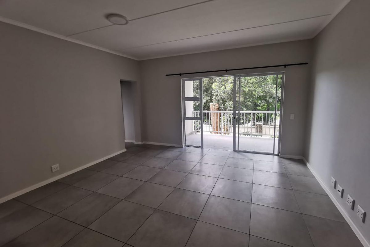 Spacious, empty living area featuring neutral grey floor tiles, recessed lighting, and large sliding glass doors providing direct access to a private balcony.