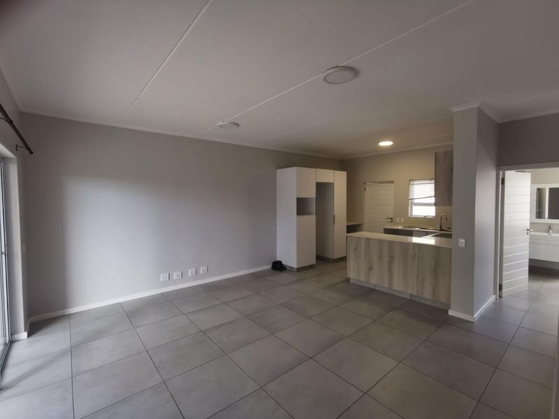 Spacious open-plan living area featuring modern tiled flooring, a functional kitchen with built-in cabinetry, and a breakfast island, perfect for contemporary apartment living.