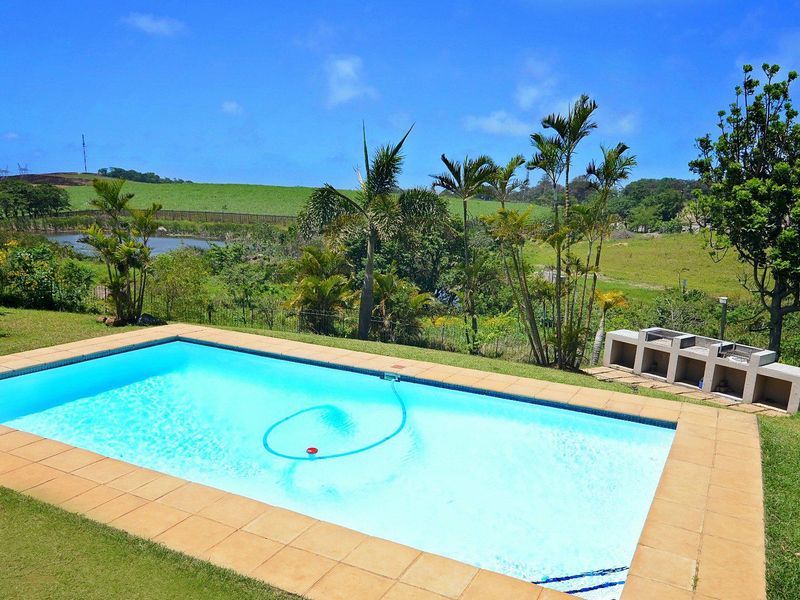 Outdoor pool area featuring a swimming pool with tiled surround and a built-in braai, set against a scenic landscape view.