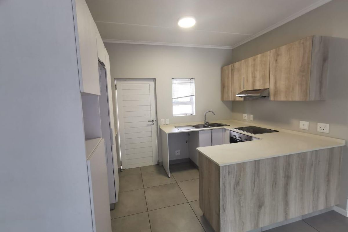 Modern kitchen featuring light wood-look cabinetry, stone countertops, integrated electric hob, oven, extractor fan, and neutral tiled flooring.