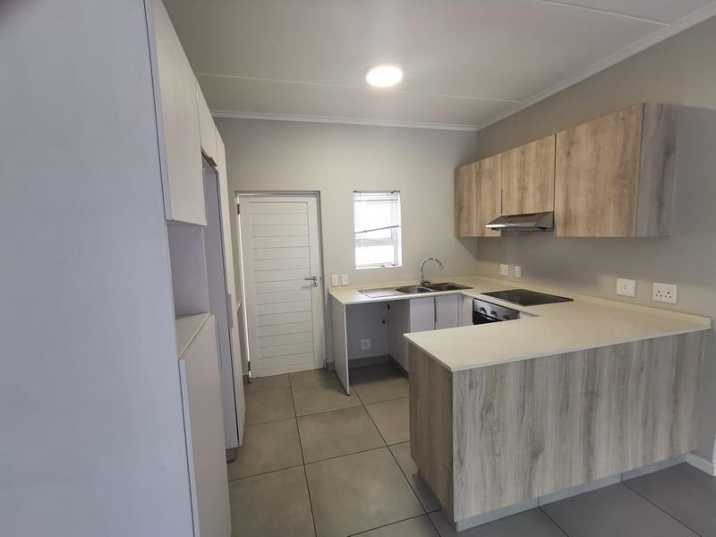 Modern kitchen featuring light wood-look cabinetry, stone countertops, integrated electric hob, oven, extractor fan, and neutral tiled flooring.