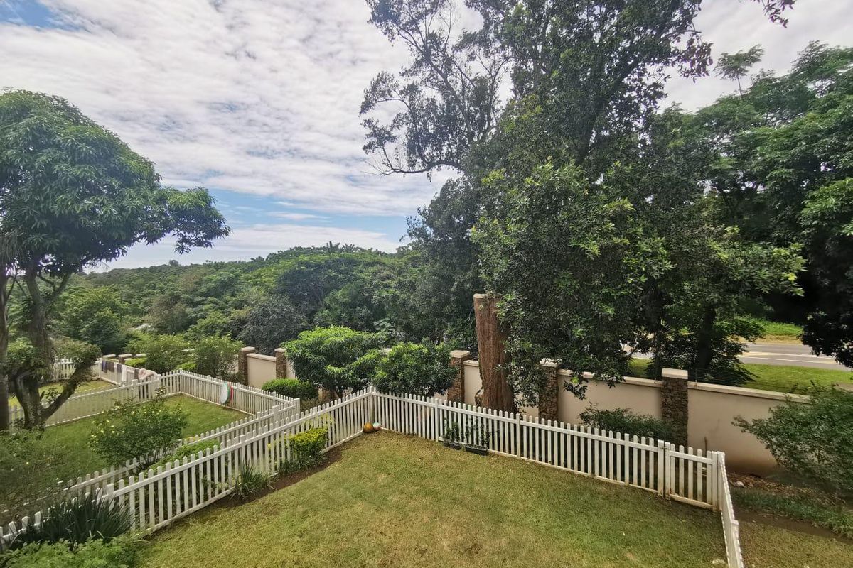 A view of a private rear garden featuring a white picket fence, manicured lawn, and a secure perimeter wall with lush surrounding greenery.