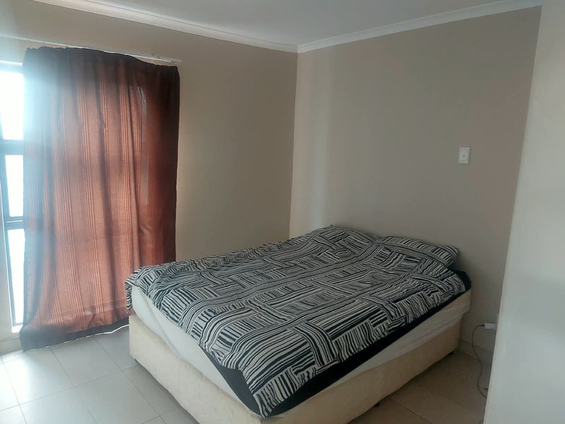 A functional bedroom featuring tiled flooring and a sliding door with curtaining, providing access to natural light.