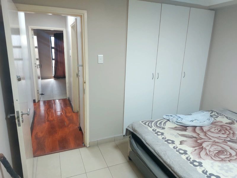 A bedroom featuring built-in cupboards and tiled flooring, with an open doorway leading to an adjacent hallway and living area.