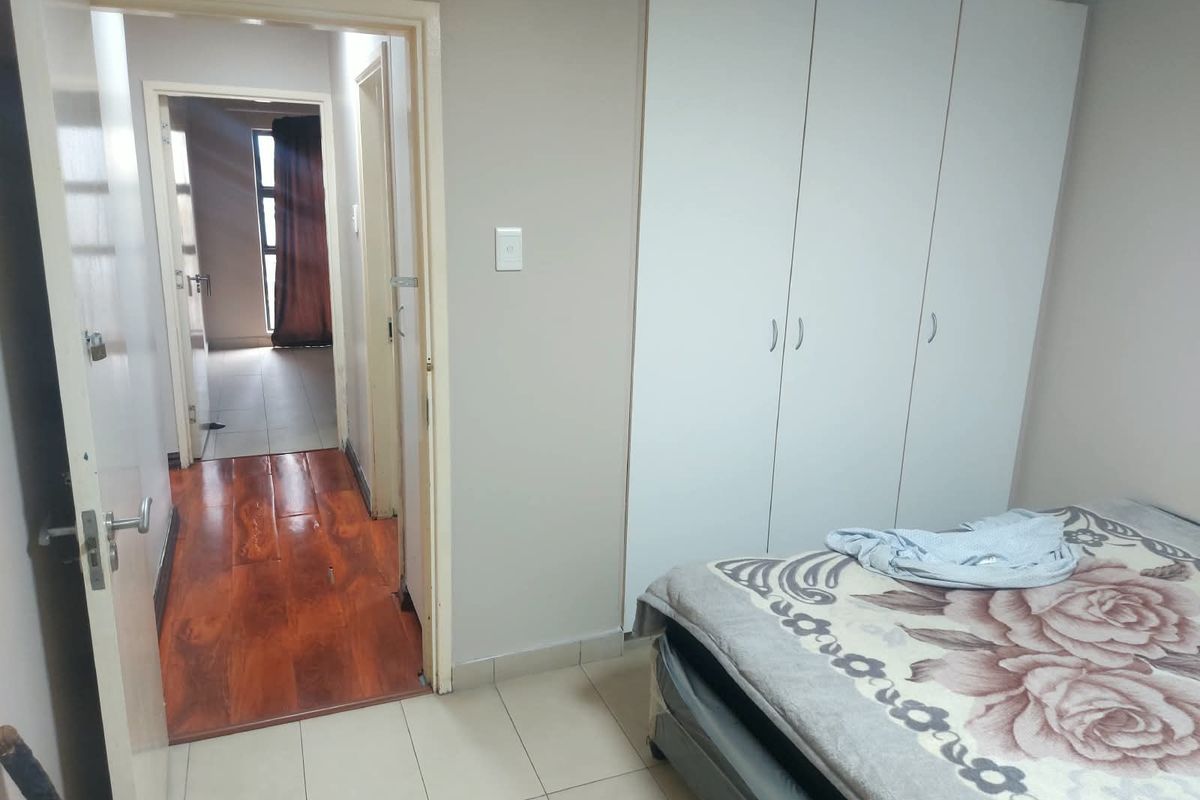 A bedroom featuring built-in cupboards and tiled flooring, with an open doorway leading to an adjacent hallway and living area.