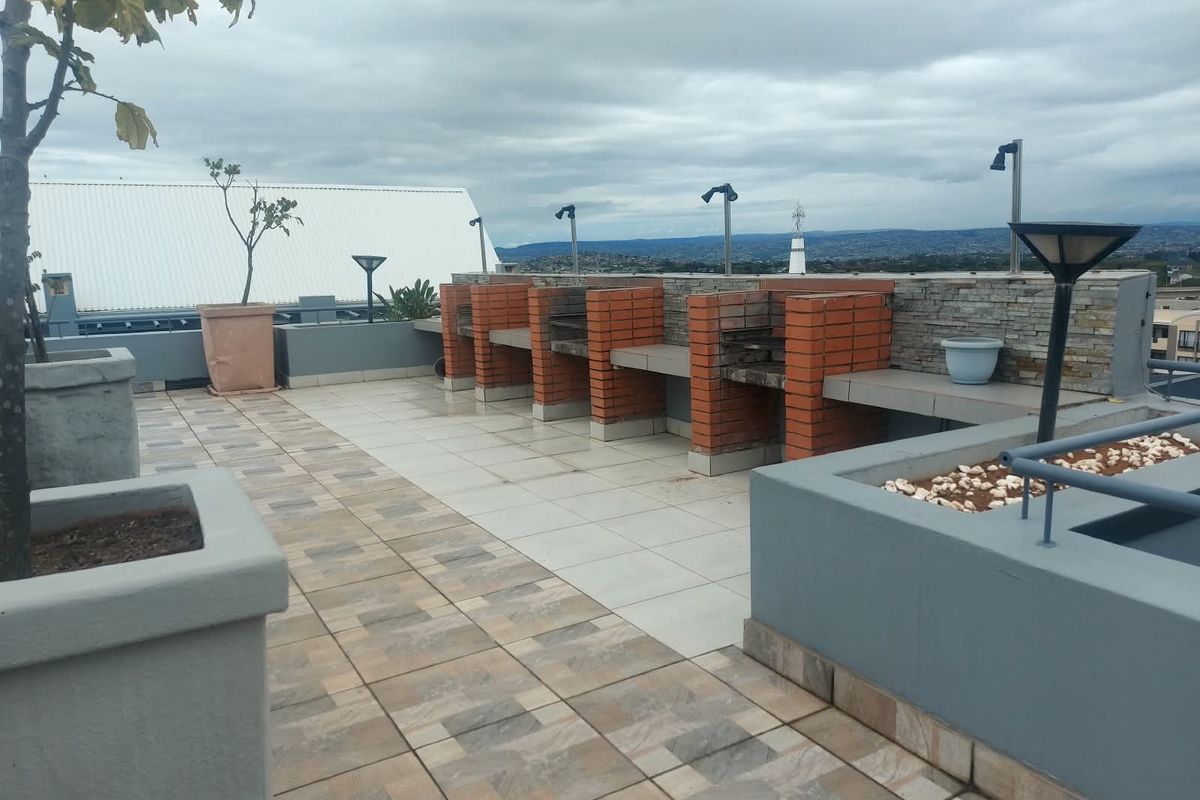 A spacious rooftop terrace featuring multiple built-in brick braai stations, tiled flooring, and integrated planters with panoramic views.