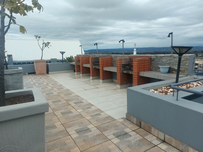 A spacious rooftop terrace featuring multiple built-in brick braai stations, tiled flooring, and integrated planters with panoramic views.