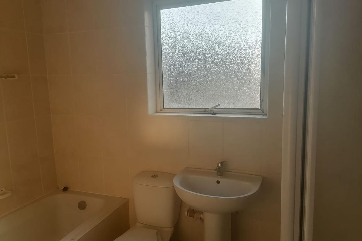 A functional bathroom featuring a bathtub, pedestal sink, and toilet with tiled walls and a frosted glass window for privacy.
