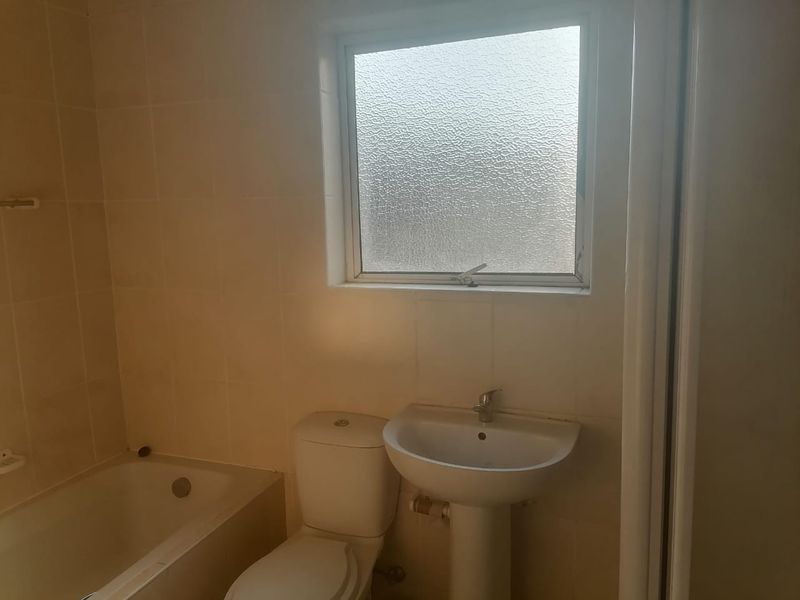 A functional bathroom featuring a bathtub, pedestal sink, and toilet with tiled walls and a frosted glass window for privacy.