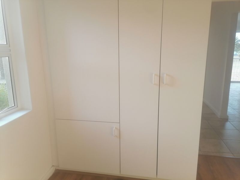 A clean, empty bedroom featuring built-in cupboards, neutral white walls, and a combination of tiled and laminate flooring.