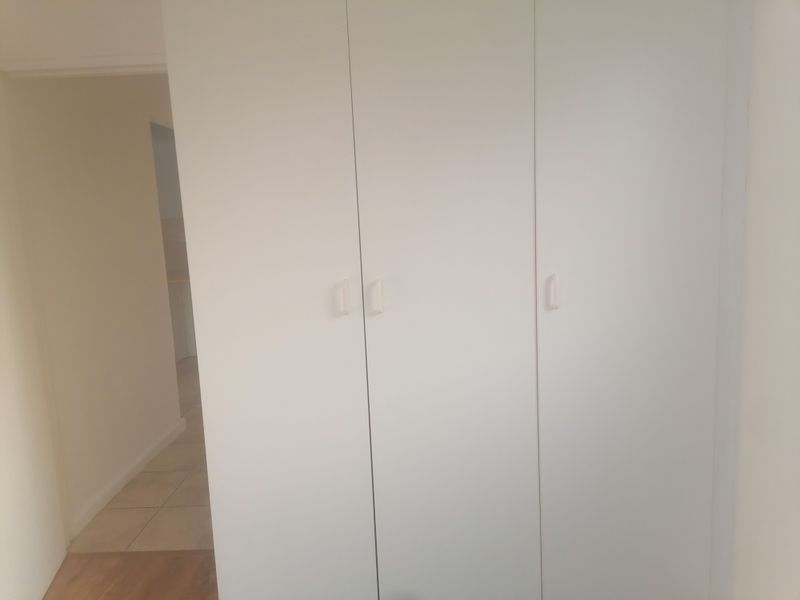 A bedroom interior featuring a white built-in wardrobe with simple handles, showing a view into an adjacent tiled hallway.