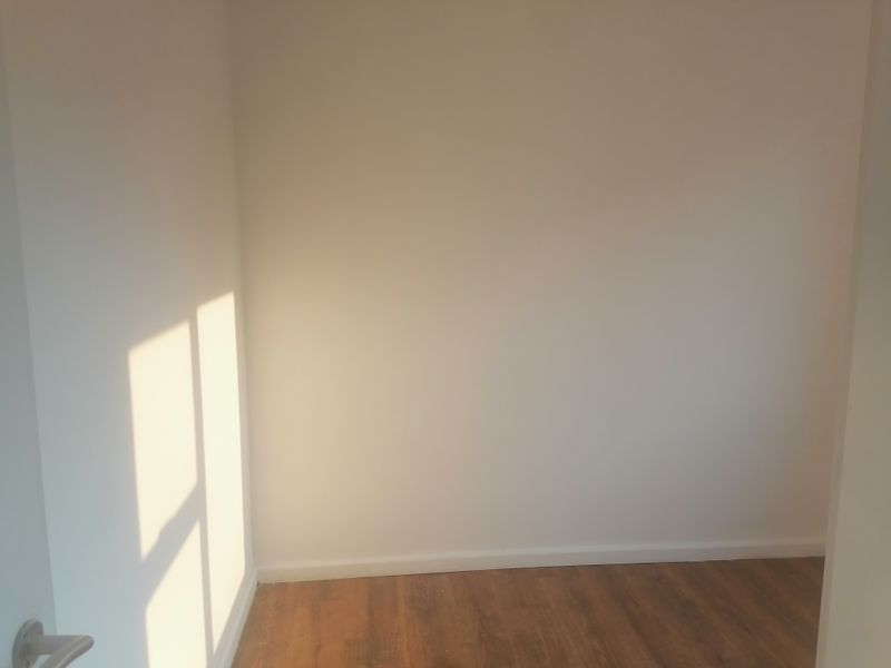 An empty bedroom featuring neutral walls and wood-look laminate flooring, illuminated by natural sunlight.