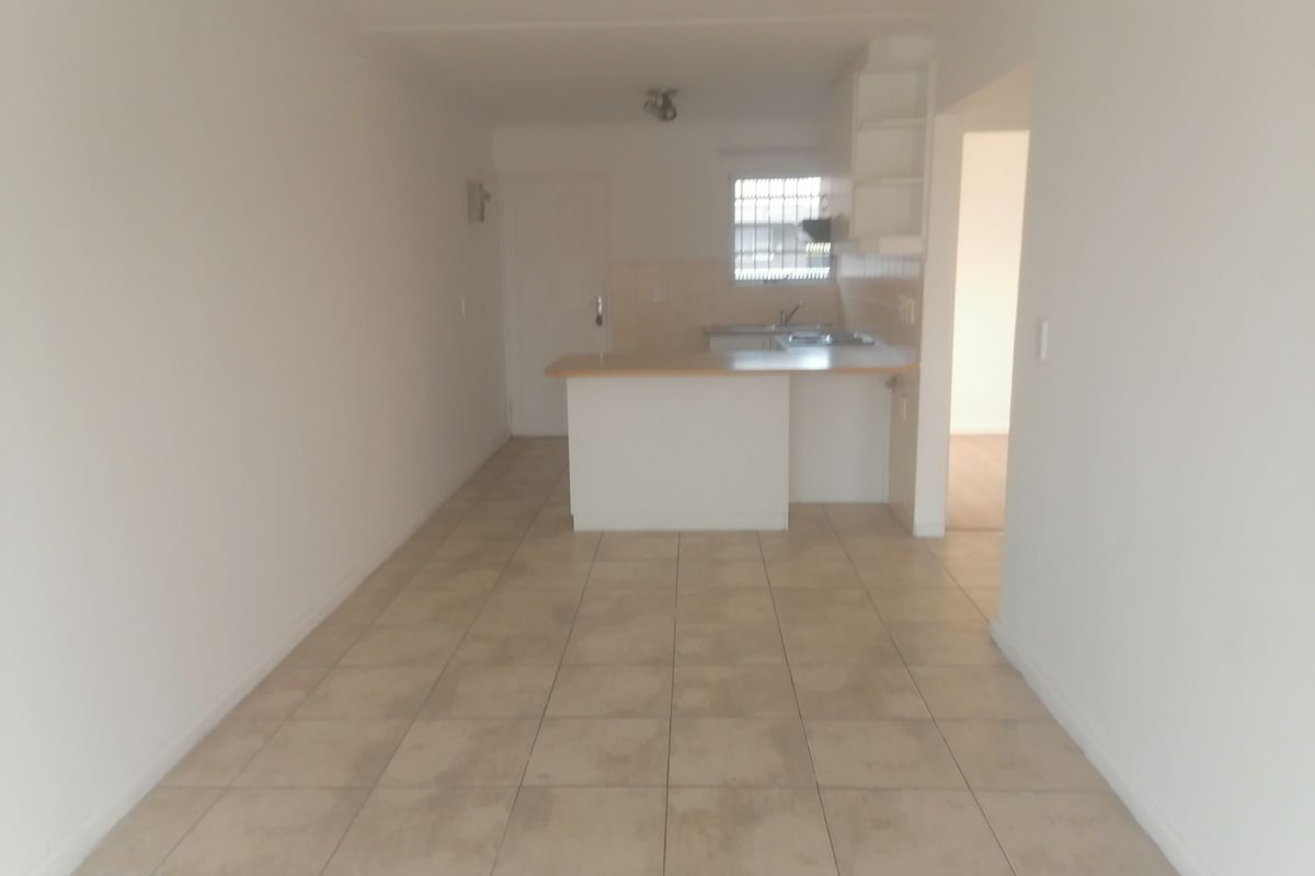 An open-plan living and kitchen area featuring tiled flooring, a breakfast bar, and built-in kitchen cabinetry.