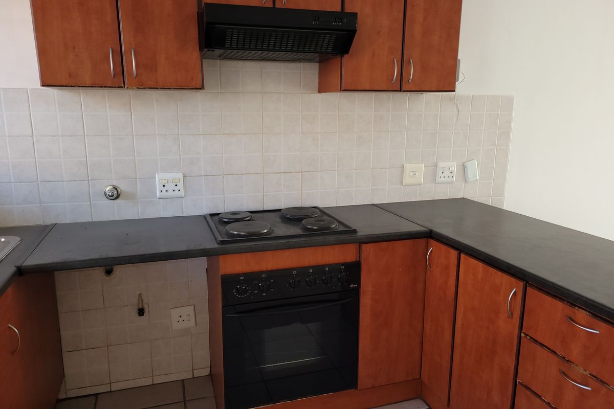A functional kitchen featuring wooden cabinetry, dark laminate countertops, a built-in oven, and an electric hob with an extractor fan.