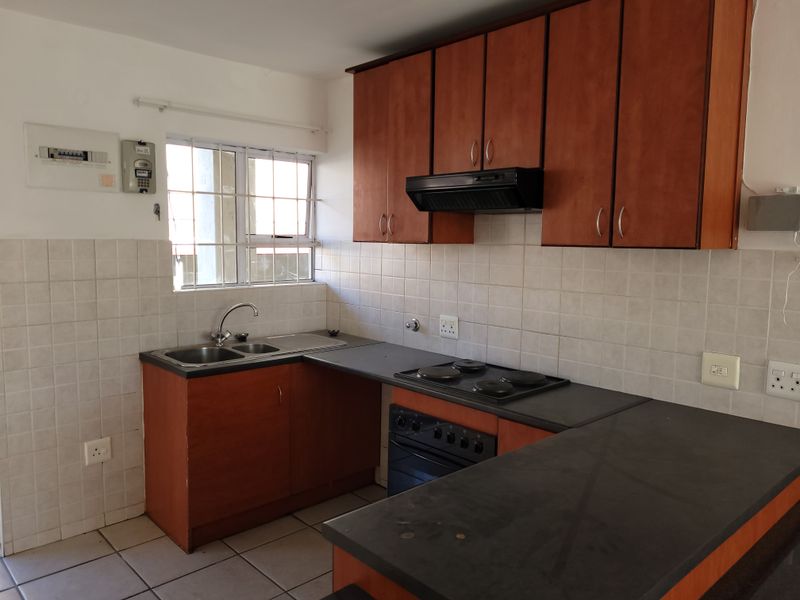 A functional kitchen featuring wooden cabinetry, dark laminate countertops, a built-in oven with hob, and tiled splashbacks in a clean, vacant space.