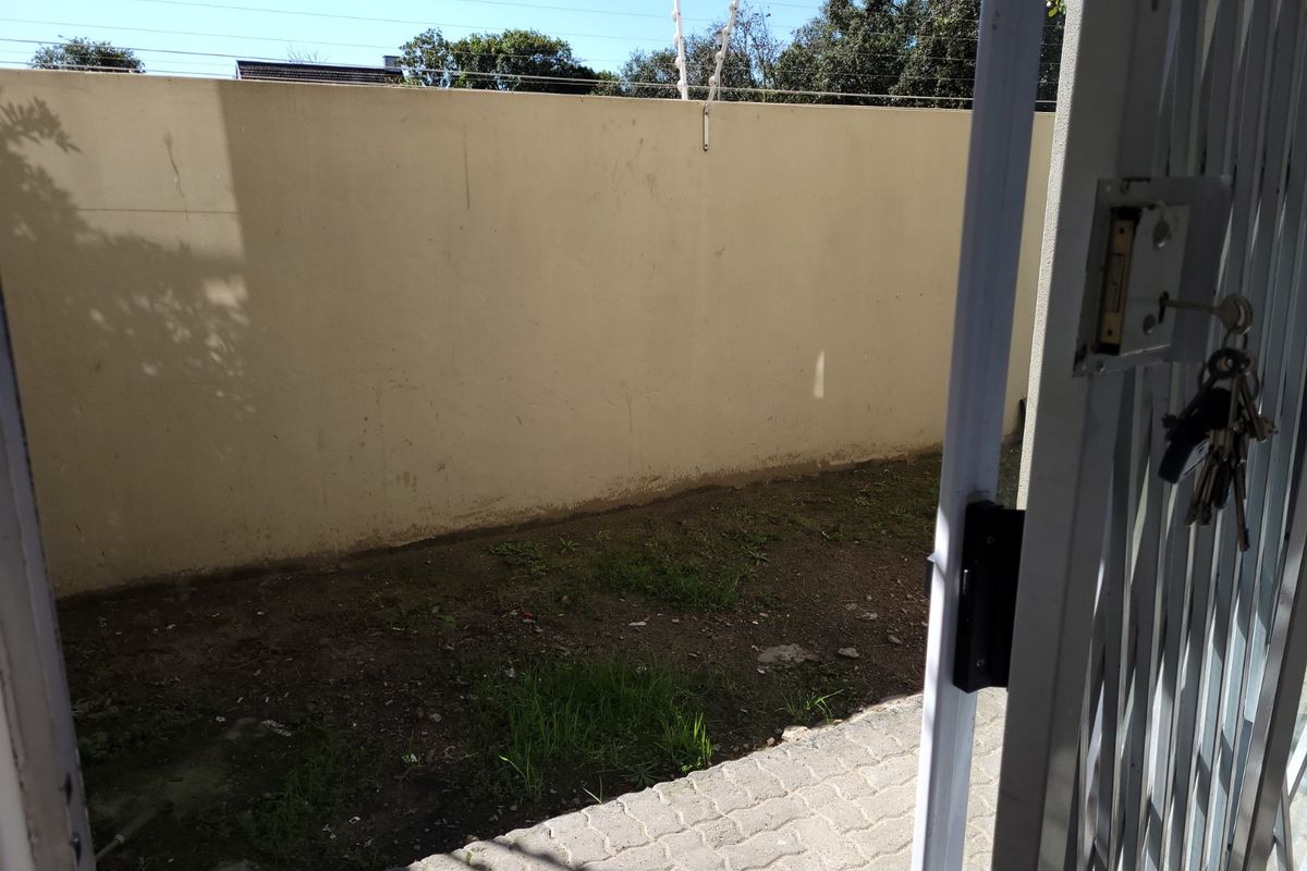 A private rear courtyard area featuring paved flooring, a perimeter wall with electric fencing, and an unlandscaped garden space.