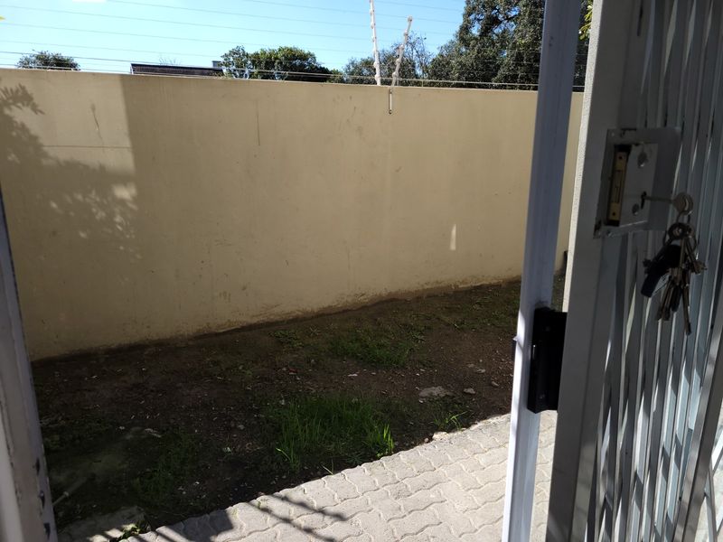 A private rear courtyard area featuring paved flooring, a perimeter wall with electric fencing, and an unlandscaped garden space.