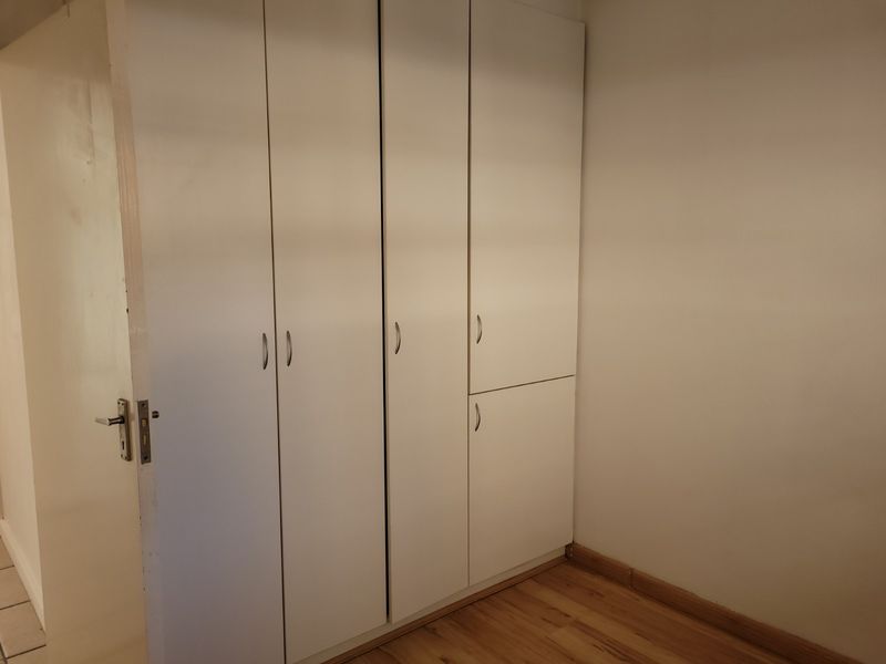 A clean, empty bedroom featuring neutral white built-in cupboards and warm-toned laminate flooring, providing a versatile space ready for personalization.