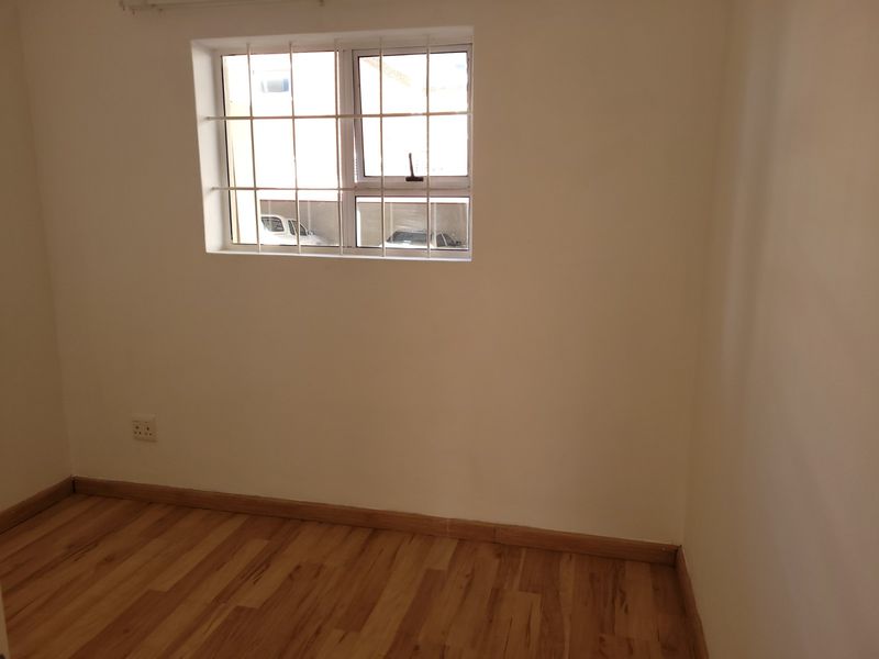 An empty bedroom featuring laminate flooring, neutral walls, and a window fitted with security bars.