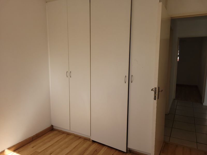 A bedroom featuring built-in cupboards and laminate flooring, with a view into the adjacent tiled hallway.