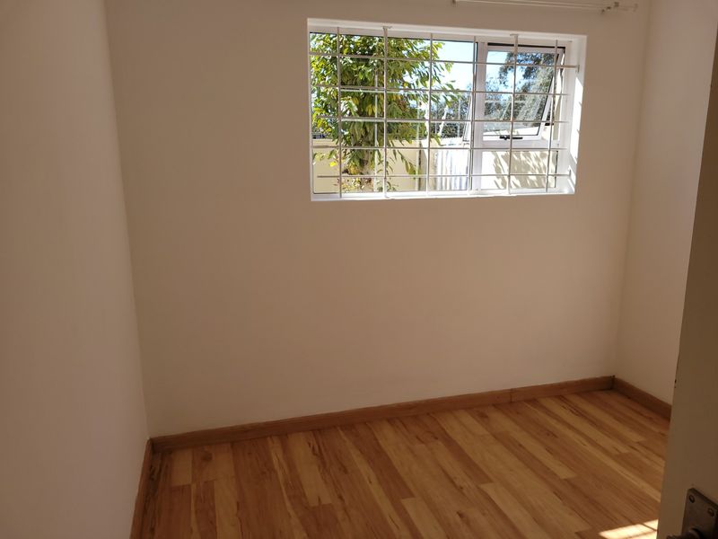 A bright, empty bedroom featuring laminate wood flooring and a window fitted with security bars.