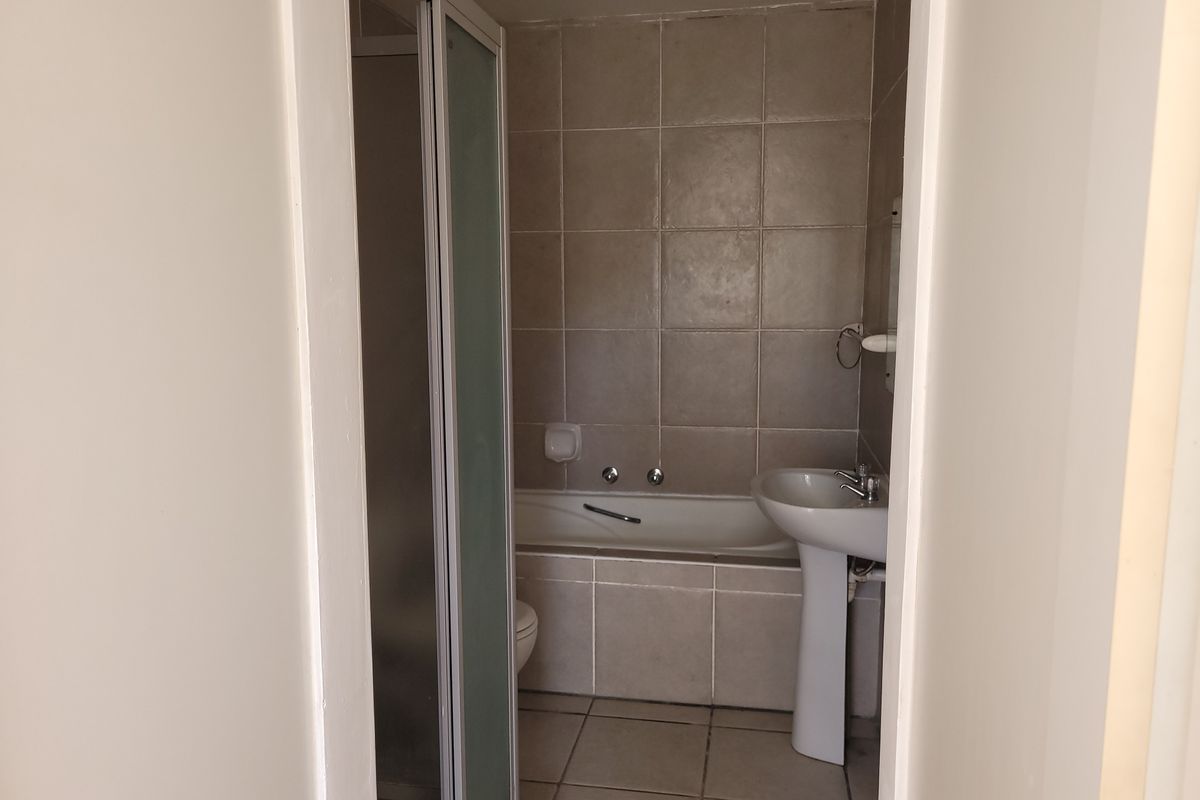 A functional bathroom featuring a pedestal basin, a built-in bathtub, and a separate shower enclosure with neutral wall and floor tiling.