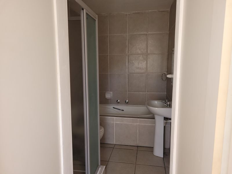 A functional bathroom featuring a pedestal basin, a built-in bathtub, and a separate shower enclosure with neutral wall and floor tiling.