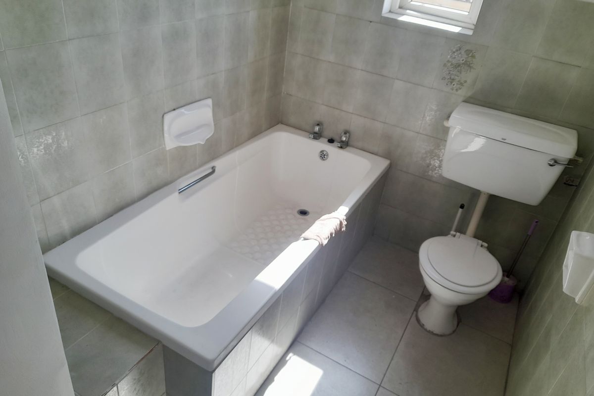 A dated bathroom featuring a standard bathtub, toilet, and neutral ceramic tiling throughout. The space is ready for modernization and renovation.