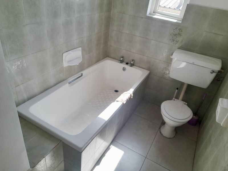 A dated bathroom featuring a standard bathtub, toilet, and neutral ceramic tiling throughout. The space is ready for modernization and renovation.