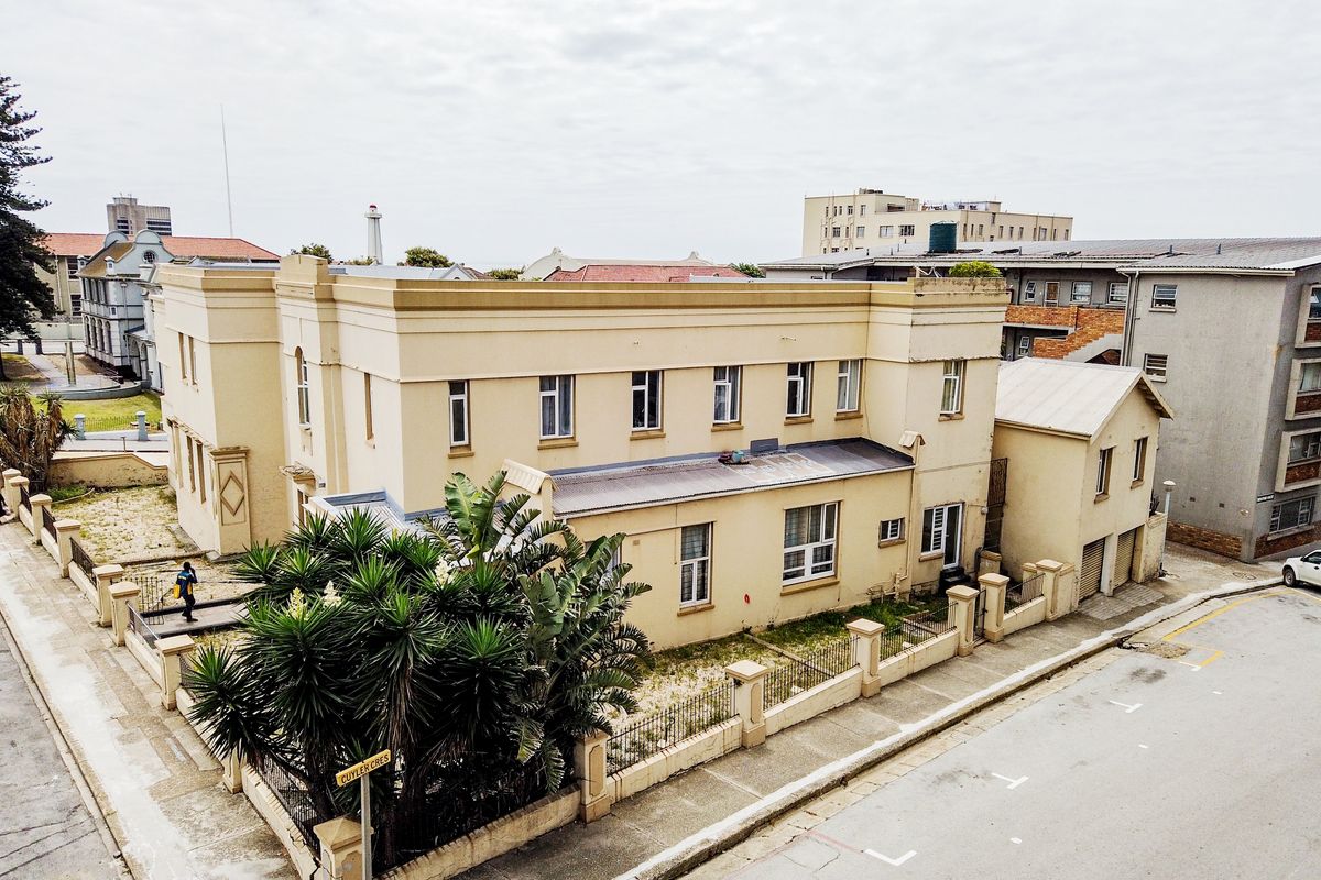 Aerial view of a multi-story apartment building featuring a perimeter wall, metal fencing, and a concrete driveway in an urban setting.