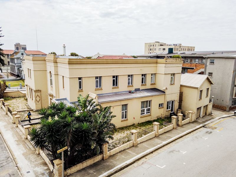 Aerial view of a multi-story apartment building featuring a perimeter wall, metal fencing, and a concrete driveway in an urban setting.