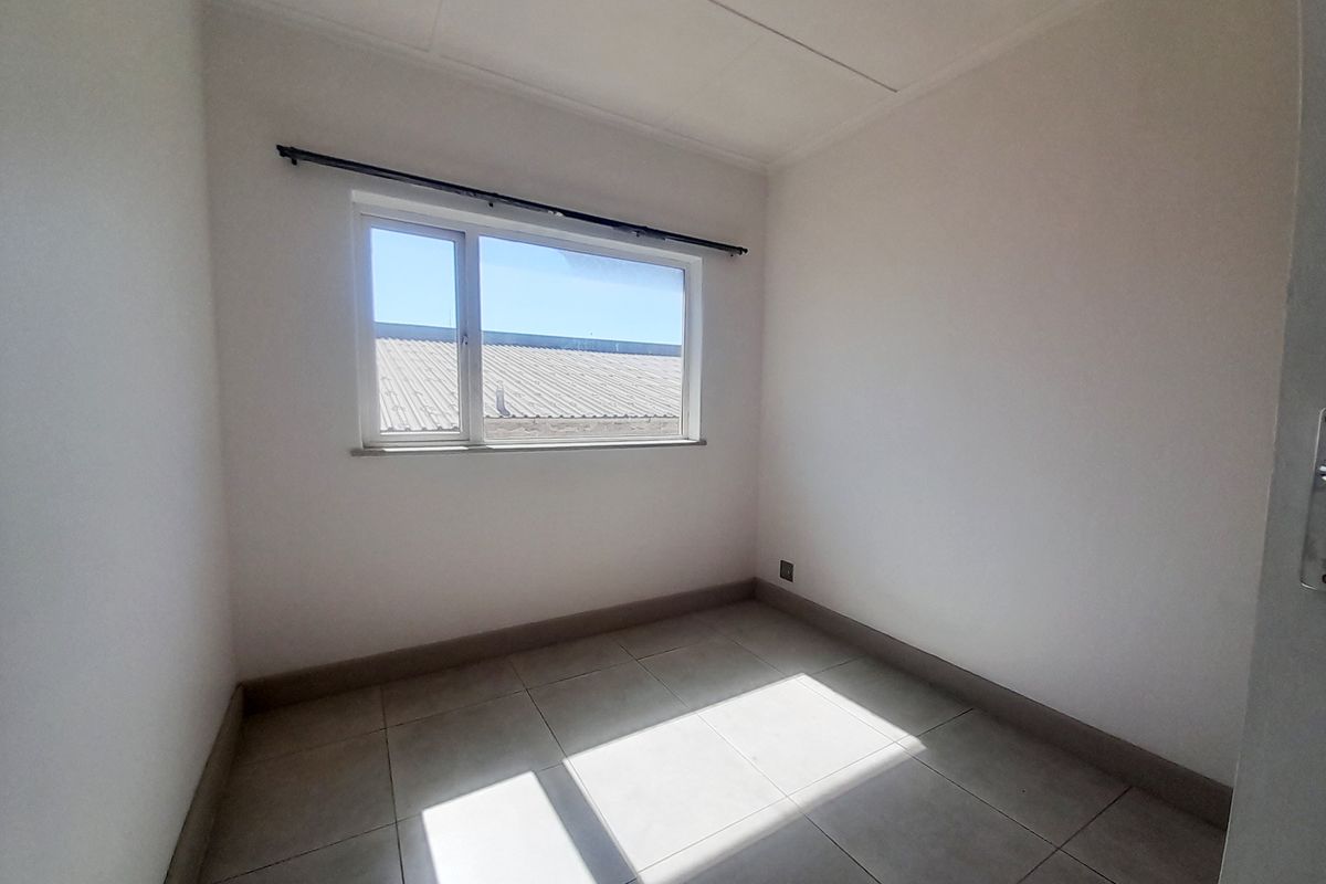 An empty bedroom featuring neutral tiled flooring, white walls, and a window with a fitted curtain rod.